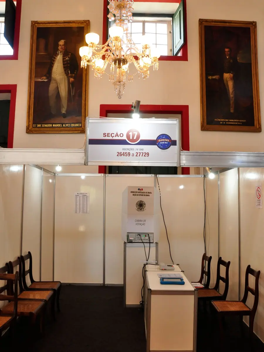 Placa com a faixa de números de inscrição atendida pela seção, cabine de votação e mesa receptora, onde o eleitor é conferido antes de votar.